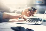 руки: одна тримає банківську картку, а інша вводить текст на клавіатурі комп`ютера